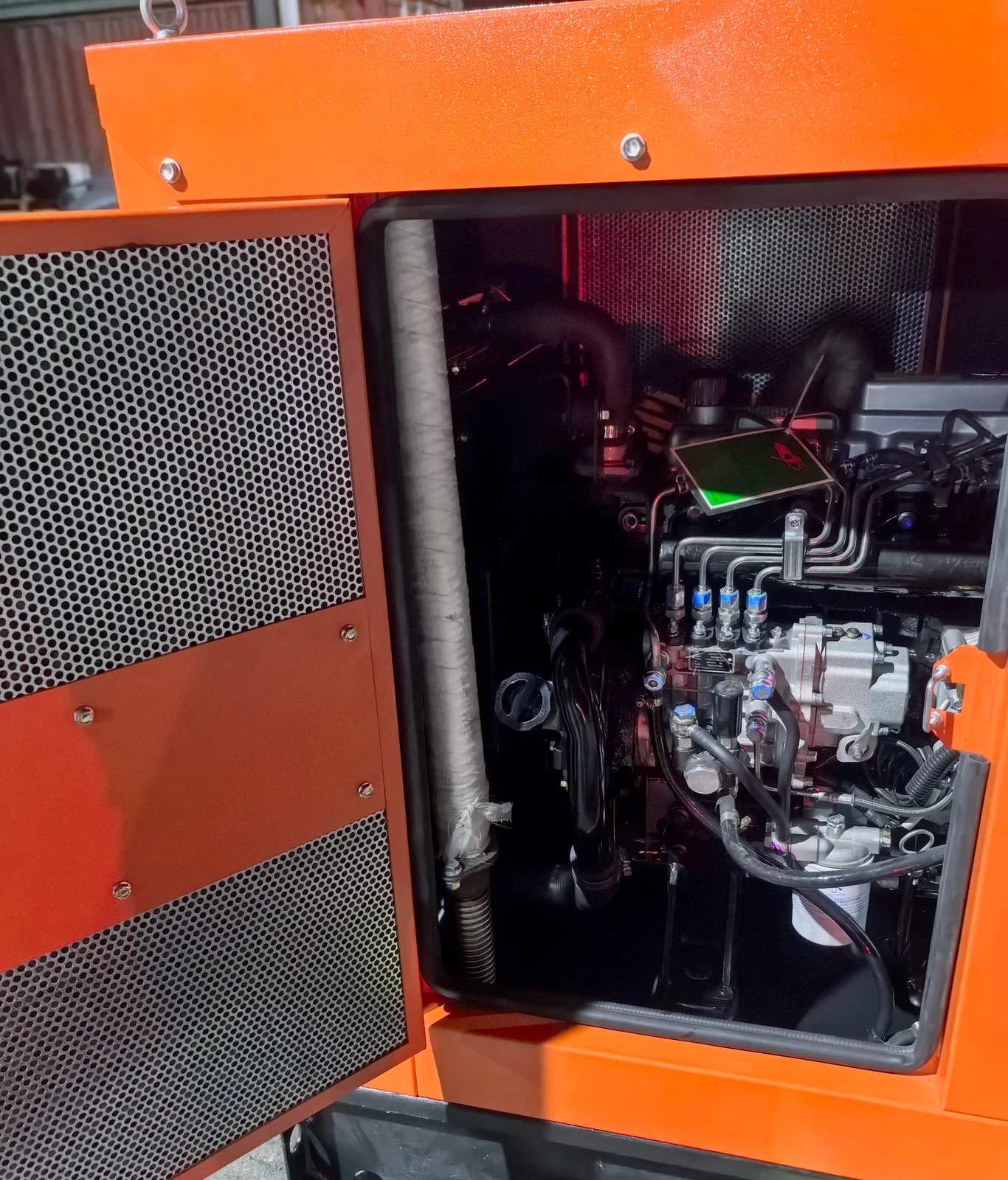 Open side service door of a BEAR enclosed generator set showing the perforated intake louvre on the door, the heat-wrapped exhaust pipe running up inside the canopy, the engine and a lifting eye on the canopy corner